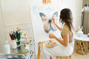 Bir sanat atölyesi sırasında tuvale güzel bir tablo çizen genç bir kadın ressamın arka görüntüsü.