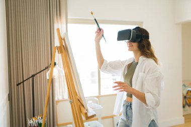 Sanal gerçeklik teknolojisini kullanarak VR gözlük kullanarak resim yapan heyecanlı genç bir kadın.
