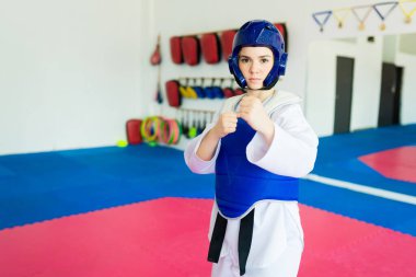 Dövüş sanatlarında koruyucu teçhizatlı bir kadın dövüşçü spor yaparken poz verir.