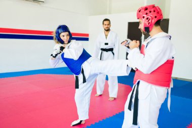 Kasklı güçlü genç bir kadın karate antrenmanı sırasında bir erkek dövüşçüyle antrenman yapıyor.