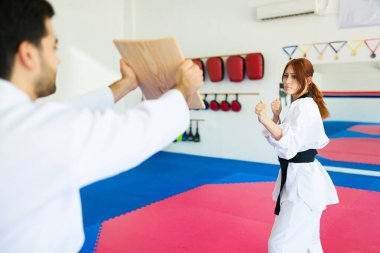 Tekvando dersinde güçlü genç bir kadın bir karate eğitmeniyle tekmeliyor ve gücünü gösteriyor.