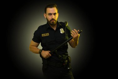 Stresli polis memuru bir suçluya bakarken göz teması kuruyor ve copunu tutuyor.
