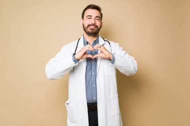Çekici erkek doktor gülümseyerek elleriyle kalp yapıyor ve hastalarla olan işini seviyor. 