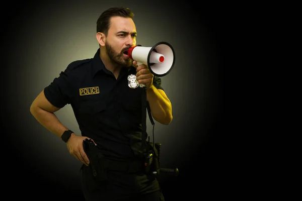 Angry caucasian police officer reaching for his gun and screaming with a megaphone