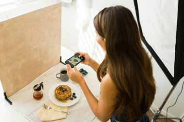 Profesyonel bir stüdyoda sosyal medya için akıllı telefonuyla yemek fotoğrafı çeken bir kadın nüfuzlu kişi.
