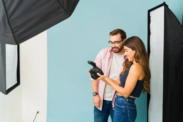 Cheerful photographer and man model laughing while checking the professional photos on the camera after a photo shoot