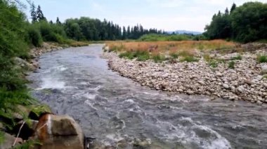 Küçük bir nehir taşların üzerinden dağların arka planına doğru akar. Sonbahar arkaplanı