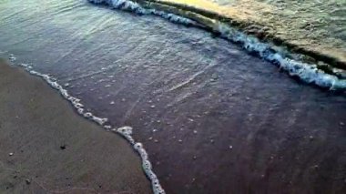 Gün batımında kumlu sahilde dalgalar ya da okyanuslar yuvarlanır.