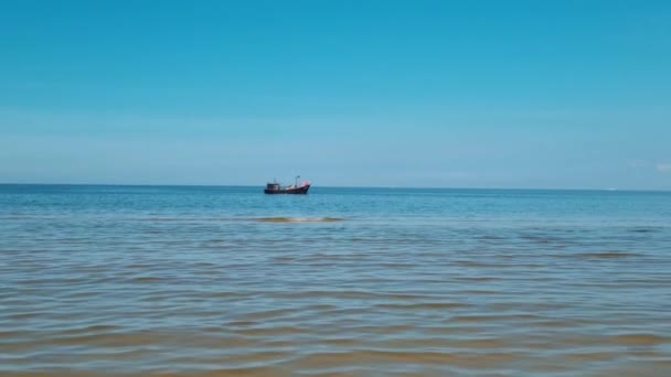 In the distance, a small fishing vessel sails in the sea or ocean. — Stock Video
