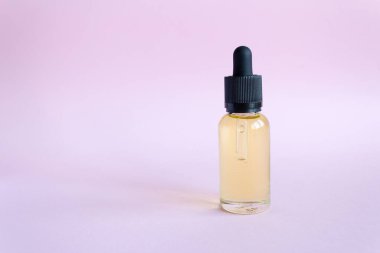 Aroma oil in a glass bottle. drip glass bottle with oil on pink background