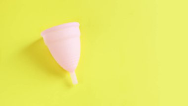 Pembe arka planda regl fincanı, kadın hijyen konsepti. Kritik günler için kadın aygıtı