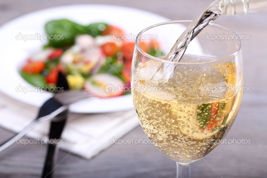 Pouring white wine into glass and food background