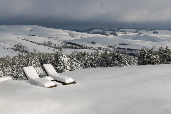 Две деревянные шезлонги, покрытые снегом, зимой на вершине холма. Солнечный день на горе Златибор в Сербии. 