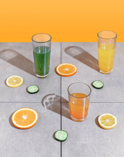 Summer refreshment aesthetic. Yellow, orange and green natural beverage in glasses with fruit and vegetable slices on tiles background.
