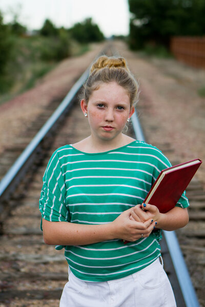 Young adolescent girl with a book on railroad tracks.