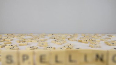 Scrabble harfleriyle heceleme kelimesi. Beyaz bir masaya dağılmış Scrabble mektupları. Güzel gri kopyalama alanı, Kamera hareketi - geri.
