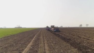 Tarla işçileri traktör römorkunun arkasında tarım yapıyor.