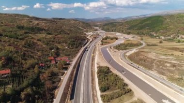 Sırbistan 'ın Pirot kenti yakınlarındaki otoyol. Alçak hava aracı geriye doğru uçuyor. Sırbistan 'ın Pirot kenti yakınlarındaki bir otoyolun insansız hava aracı görüntüsü. Bir tarafta ovalar, diğer tarafta tepeler ve evler. Trafik az, güzel bir gün. Geriye doğru pürüzsüz bir uçuş, uzaktan kumandalı hava aracı.