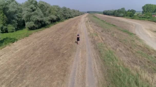 女性の距離のカメラから田舎のパス上を歩く 上のカメラ 夏の長い影 一人で暑い一日を楽しんでいる女性 リラックスするためのカジュアルな散歩 高架歩道 — ストック動画