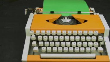 Typewriter stylish orange. Vintage mechanical typing machine. White keyboard green paper. Camera travelling above.