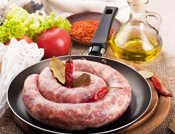 Home sausage in a frying pan, pepper and laurel sheet — Stock Photo, Image
