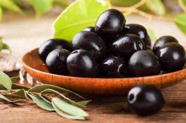 Black olives in a wooden plate and a rough board clipart
