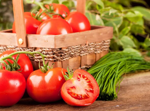 Tomates y cebollas verdes en una cesta triturada —  Fotos de Stock