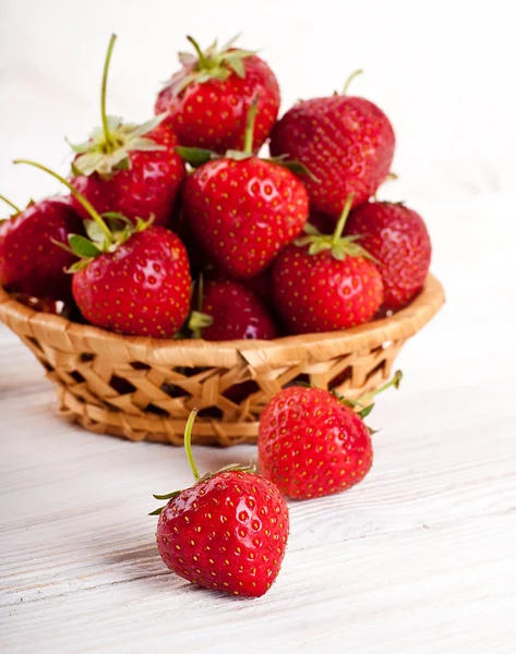 Rijpe aardbeien in een rieten mand op een wit bord — Stockfoto