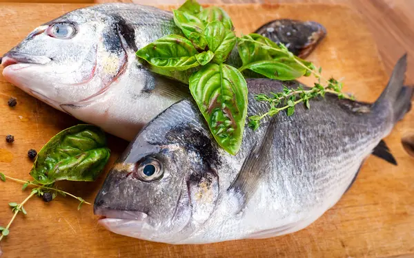 Peixe dorado com limão e especiarias em uma tábua de madeira — Fotografia de Stock