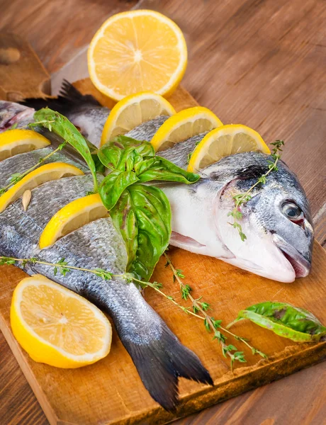 Pesce dorado con limone e spezie su una tavola di legno — Foto Stock