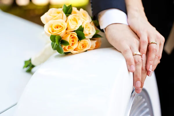 Hands of bride and groom with rings and bouquet of flowers — Stock Photo, Image