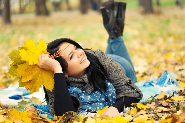 Mulher jovem que põe em folhas de outono — Fotografia de Stock