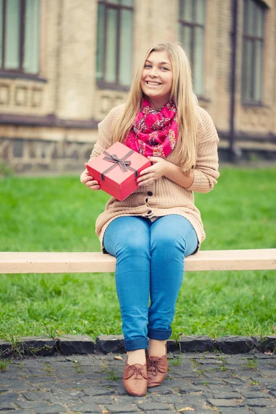 Ung kvinna med nuvarande på bänk — Stockfoto