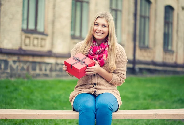 Ung kvinna med nuvarande på bänk — Stockfoto