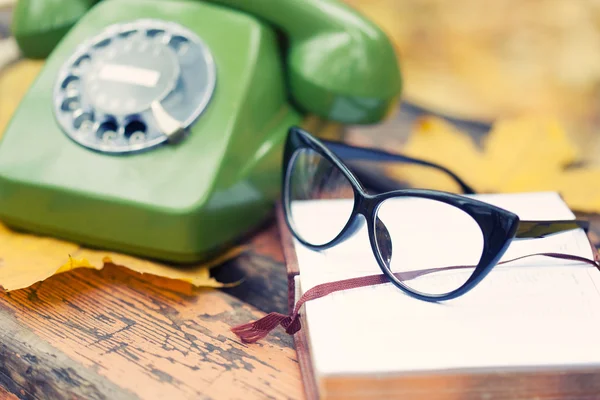 Zelené vinobraní telefon, kniha a brýle na lavičce v podzimním parku — Stock fotografie