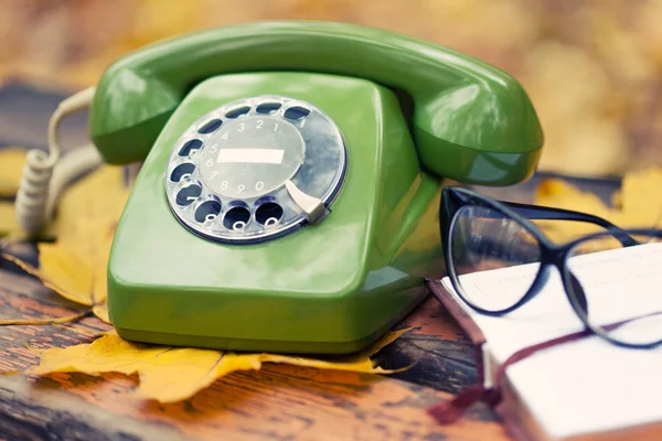 Grünes Oldtimer-Telefon, Buch und Brille auf Bank im Herbstpark — Stockfoto