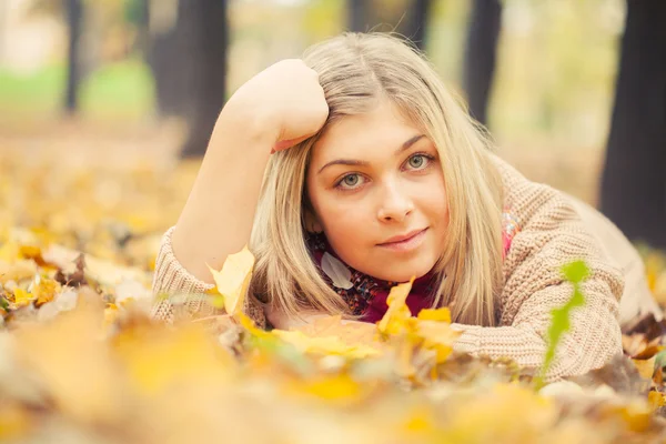 Ung kvinna fastställande på marken i höst park — Stockfoto