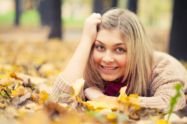 Young woman laying down on the ground in autumn park — Stock Photo, Image