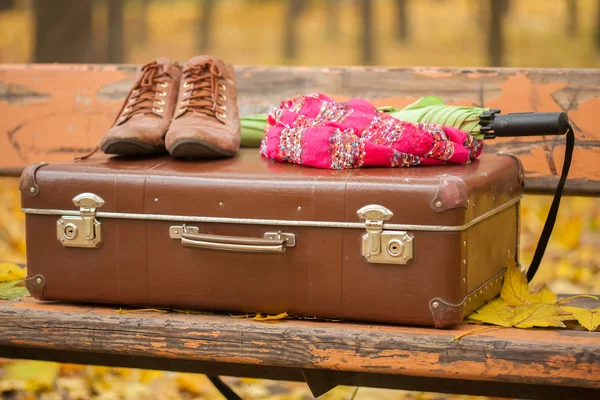 Ročník kufr, šátek, vysoké boty a deštník na lavičce — Stock fotografie