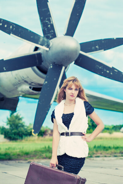 Woman with  suitcase posing against plane