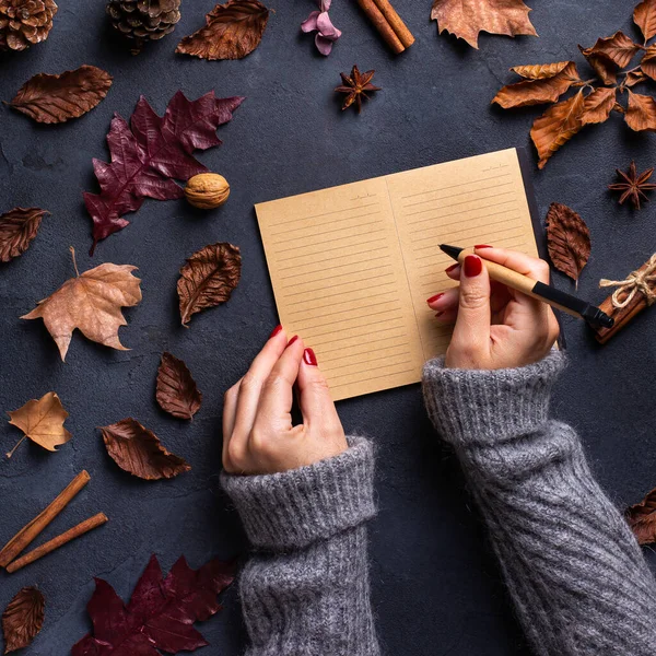 Autumn fall thanksgiving day composition with decorative dried leaves. Female hands writing in notebook. Flat lay, view from above, still life seasonal background for greeting card, copy space