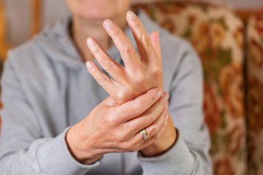 Senior woman suffering from hand and finger joint pain and inflammation. Rheumatoid arthritis, gout and carpal tunnel syndrome.