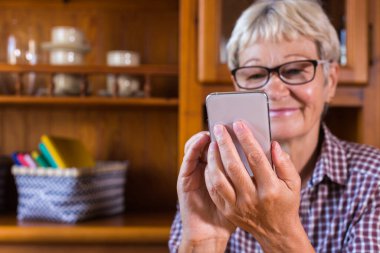 Senior woman talking with family and friends, making video call on the phone, writing a message