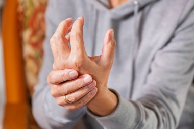 Senior woman suffering from hand and finger joint pain and inflammation. Rheumatoid arthritis, gout and carpal tunnel syndrome.