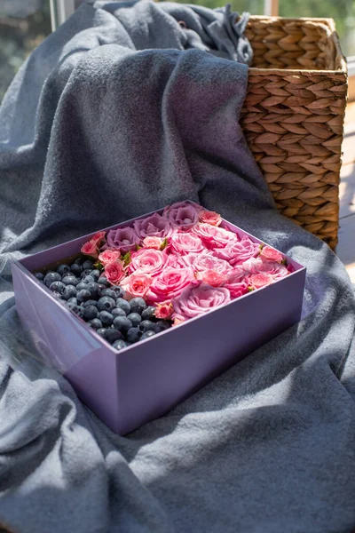 Craft square box filled with blueberries and pink roses on soft plaid background,basket neare.Fresh flowers bouquet in sunny morning.Edible gift for Valentines Day,mothers day,wedding.Copy space