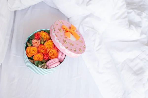 Gift box with open top full of orange roses,french macarons in bed.Fresh flowers bouquet.Floral composition.Birthday,Valentines morning with present.Honeymoon concept.Good delivery,hotel service.