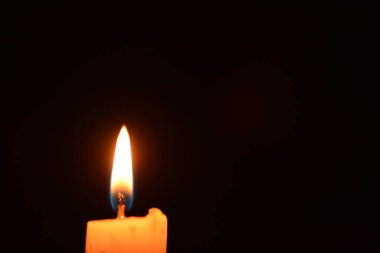 Siyah arkaplanda beyaz bir mumun üzerinde parlayan tek bir mum ışığı. Aydınlatılmış Mumların Karanlık Arkaplanda Yakın Çekimi .