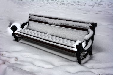 Kışın karla kaplı park bankında. Karlı soğuk hava. Kar yağdıktan sonra kış sabahı. Açık hava bankı karla kaplı.