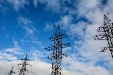Elektrik iletim hattı. Yüksek voltajlı elektrik direkleri ve açık mavi gökyüzü arka planında elektrik kabloları. Yüksek voltaj iletim hatlarının modern altyapısı. Enerji endüstrisi.