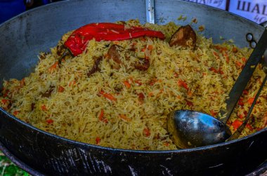 Aşçı kazanda pilav karıştırır. Güneşli bir günde, ahşap bir masada, bir kazanda geleneksel doğu pilavı. Gerçek pilav için adım adım tarif.